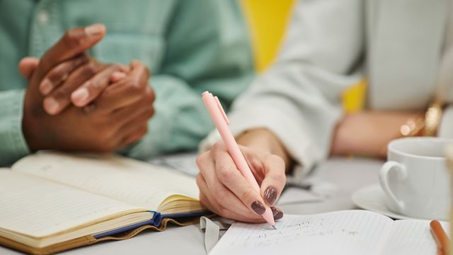 Close-up of two hands writing in notebooks with a pen during a meeting