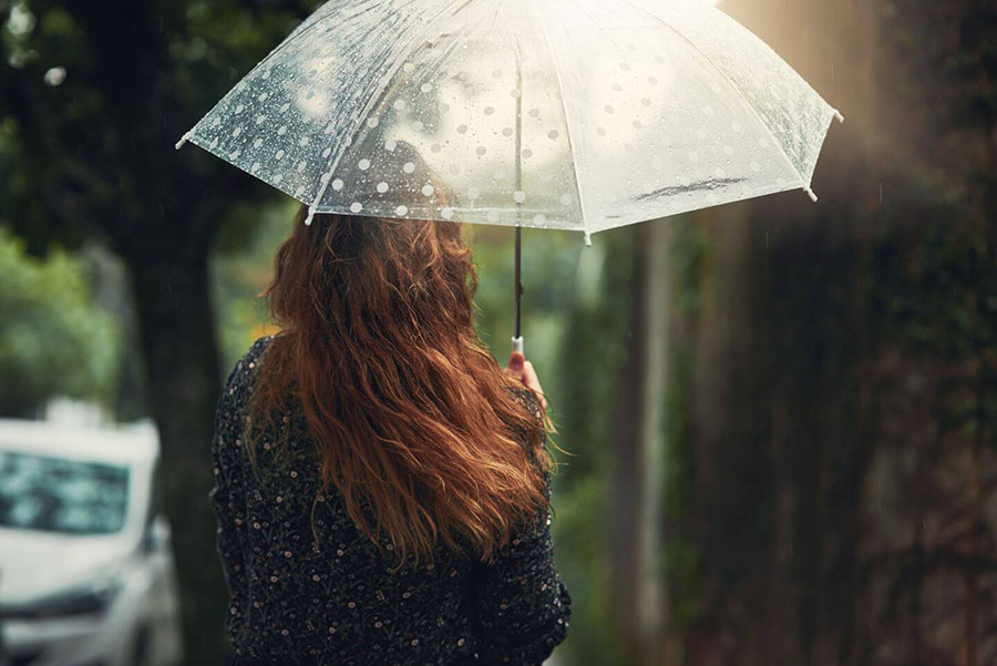 Rear view of red-haired woman holding umbrella above her head