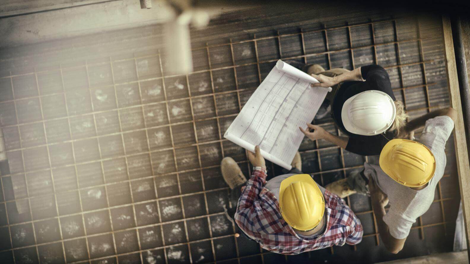 High angle view of three people with helmets, female architect, foreman and engineer on a construction site, looking down on a blueprint