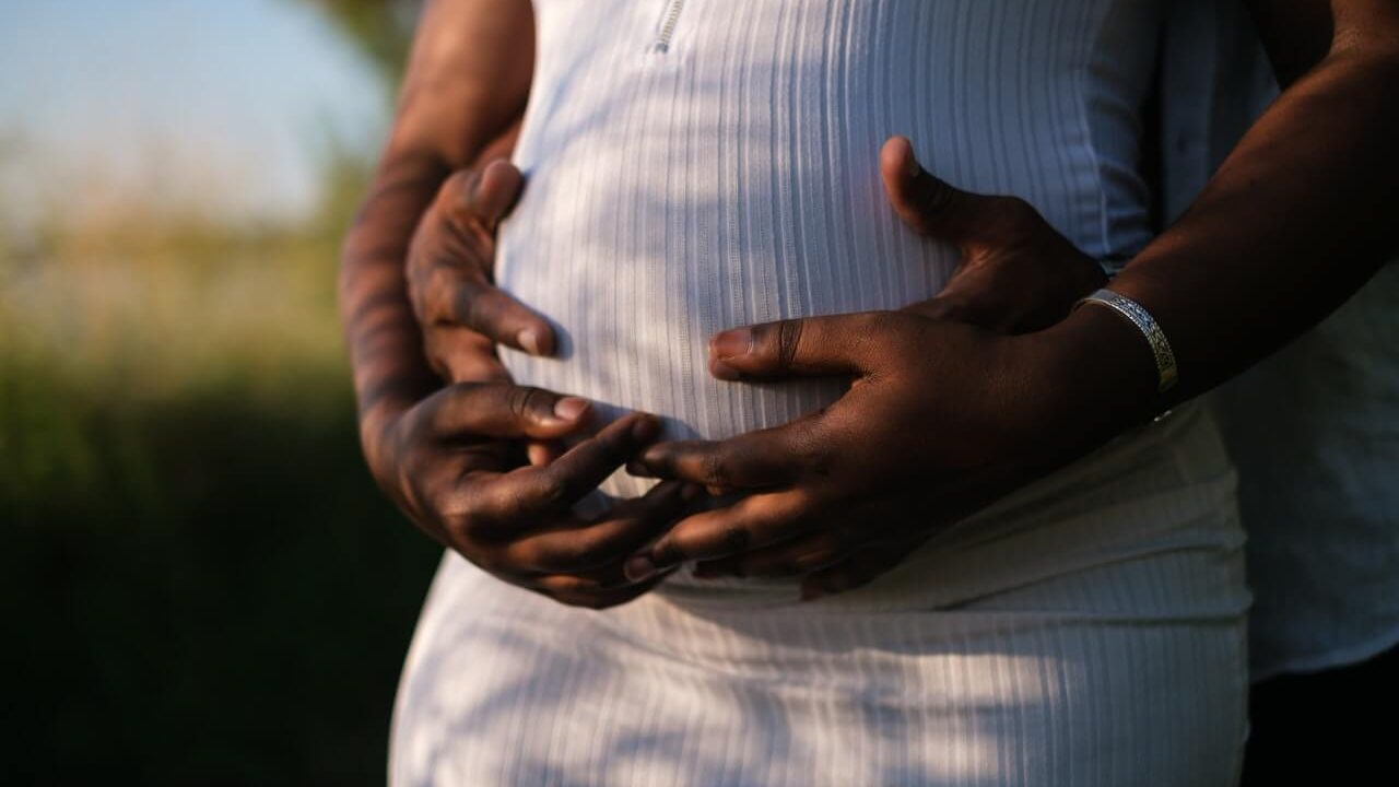 Close up of pregnant female with male hands holding the bump from behind