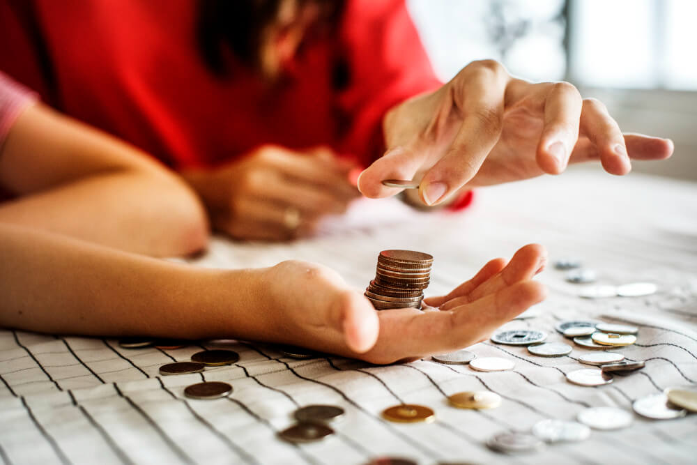 An adult female in a red jumper counting coins on a table