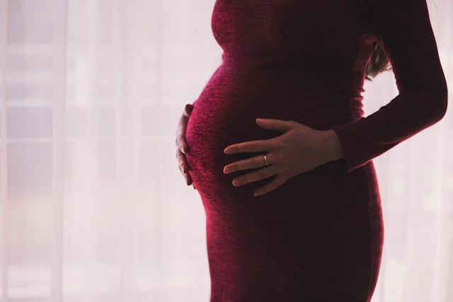 Pregnant woman in red dress holding bump