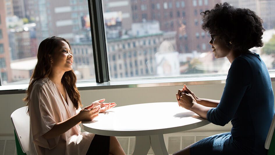 Two smartly dressed females talking across-a table