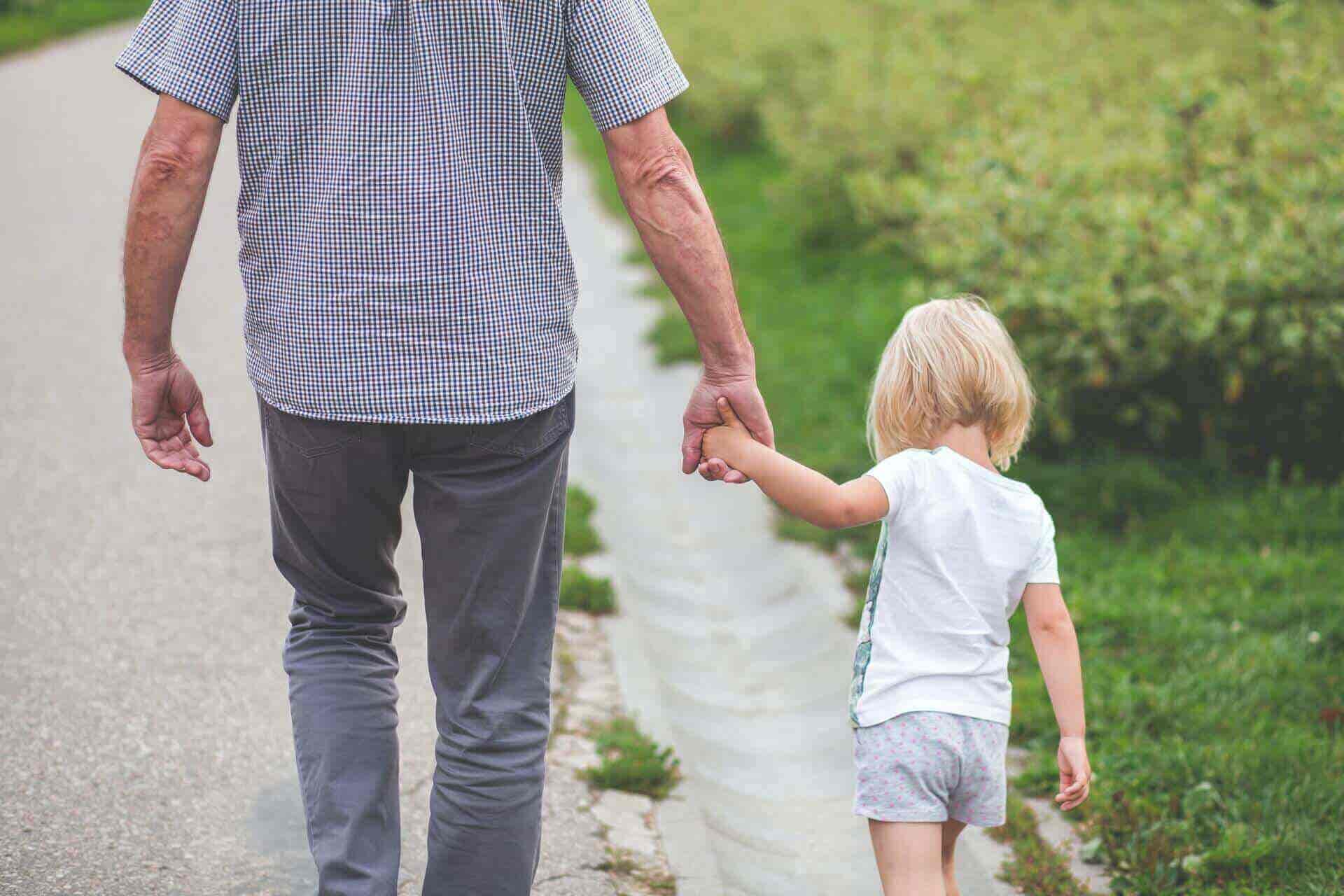 Rear view of older man holding young child's hand