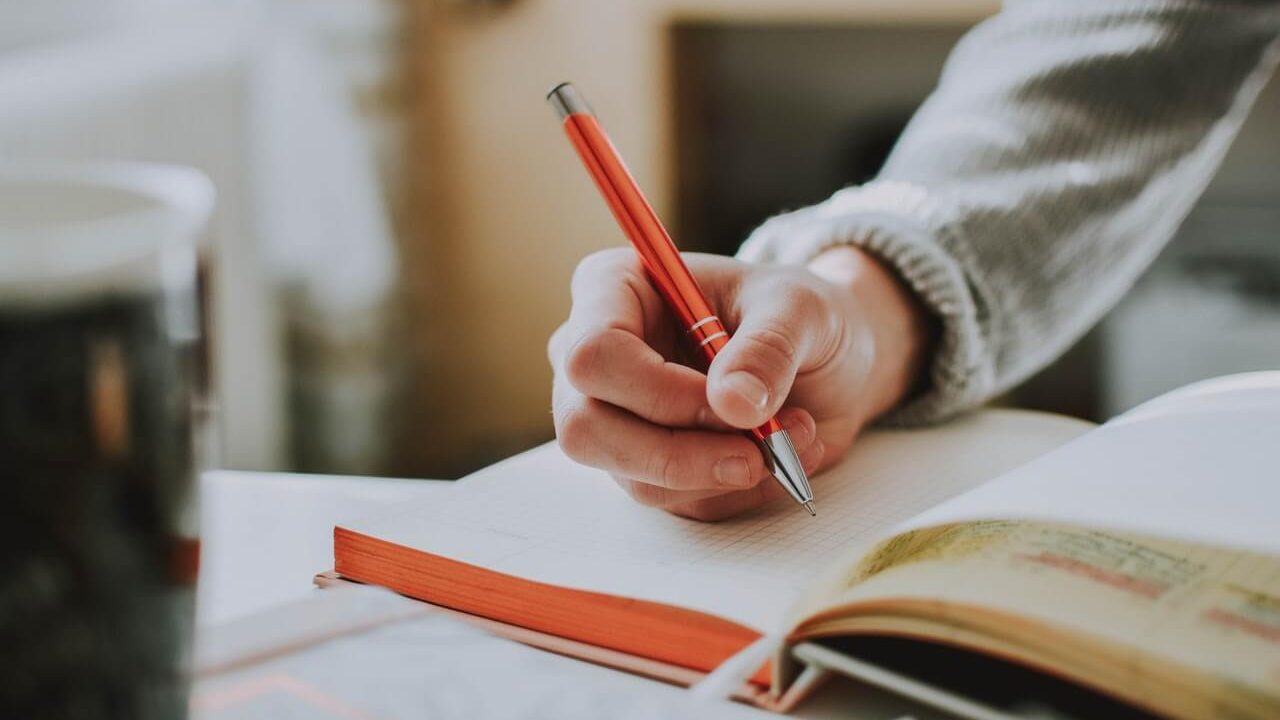Person writing in notebook with a red pen