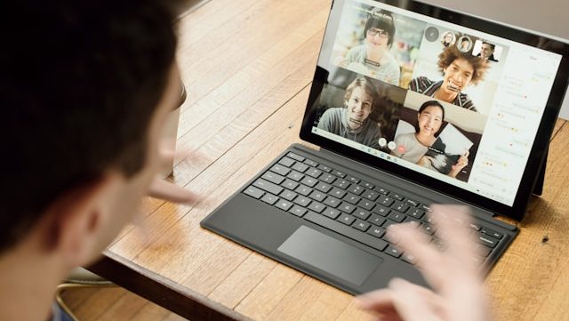 Above view of a dark haired male looking at a laptop which has a video call on the screen