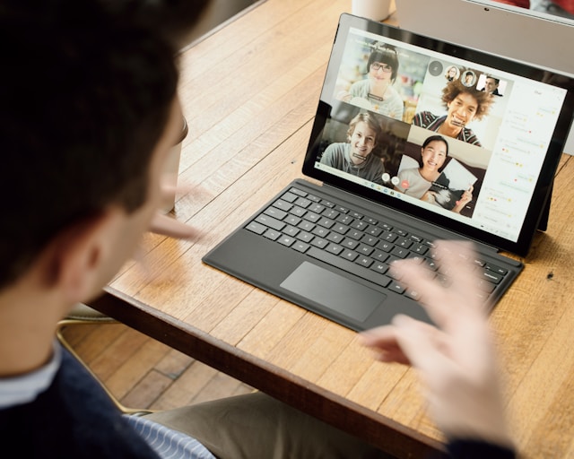 Above view of a dark haired male looking at a laptop which has a video call on the screen