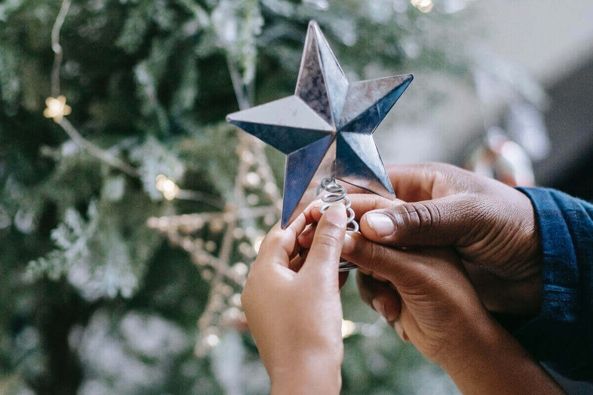 Adult male hand helping child's hand to put star on Christmas tree