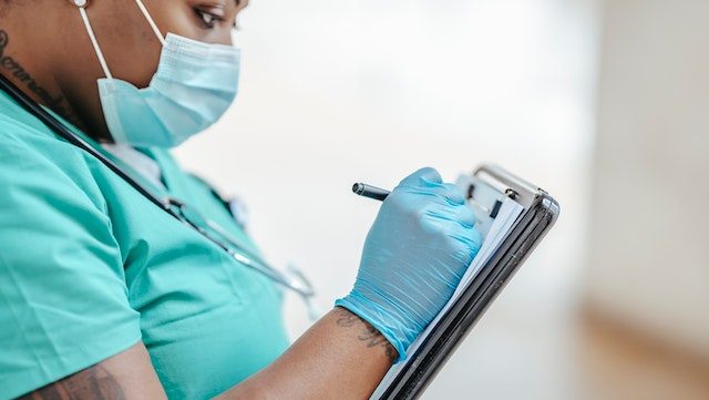 Close up of nurse writing notes on clipboard