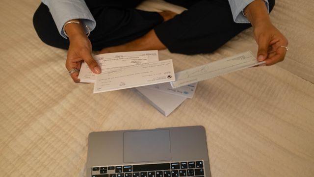 Close-up of hands holding cheques beside a laptop