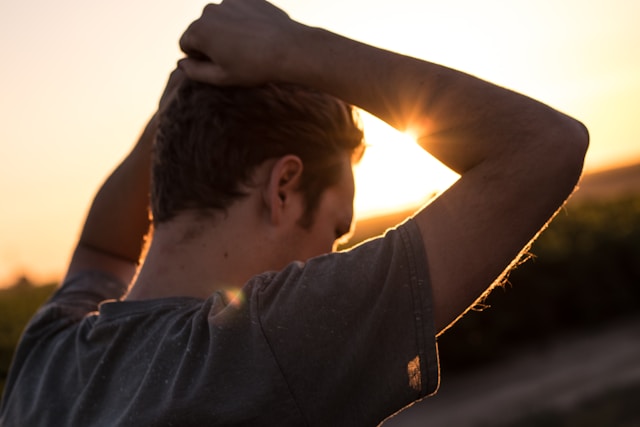 dark-haired-male-with-hands-on-head-against-sunset