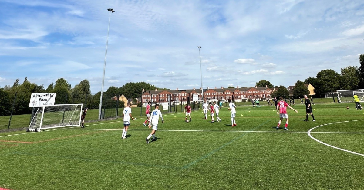 group-of-young-people-in-football-kits-playing-on-a-green-football-pitch-against-blue-sky