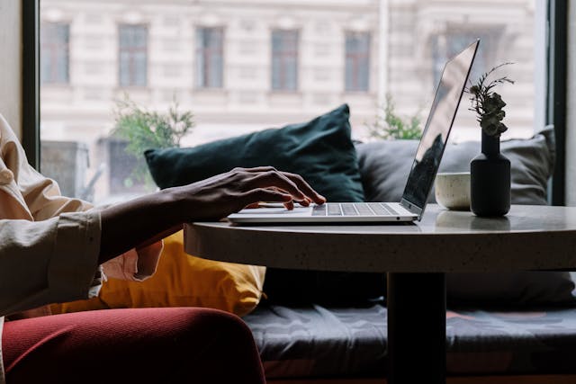 Side view of a person dressed in a formal suit sitting at a desk, with their hands resting on a laptop keyboard