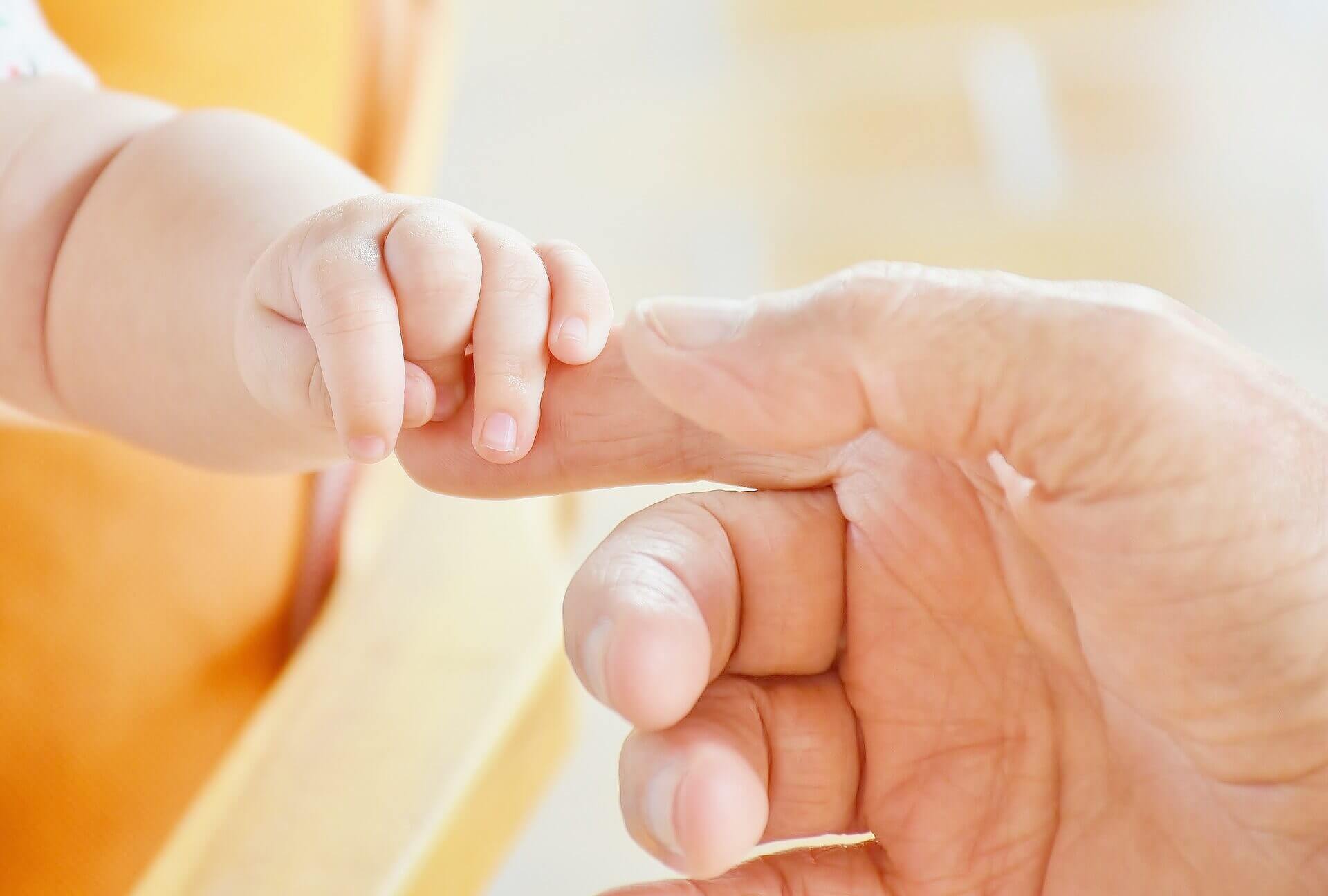 Close up of a baby holding an adult's finger