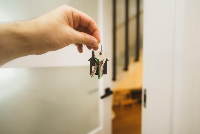 A hand holding a key to a door in front of a neutrally decorated modern room