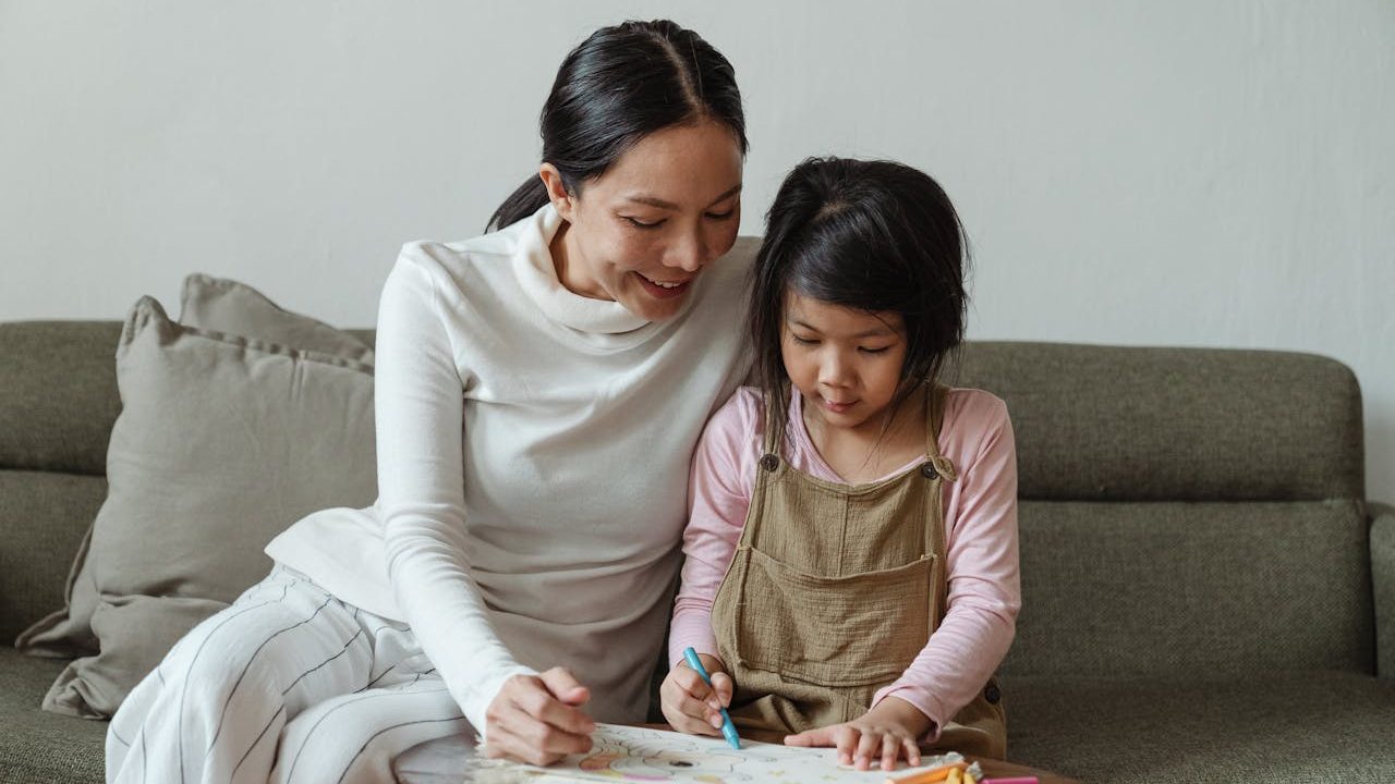 Woman and young girl sitting on a neutral coloured sofa, drawing on paper
