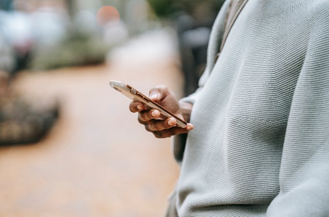 A side view of a woman holding a mobile phone in one hand. She is wearing a pale blue jumper. The background is softly blurred.