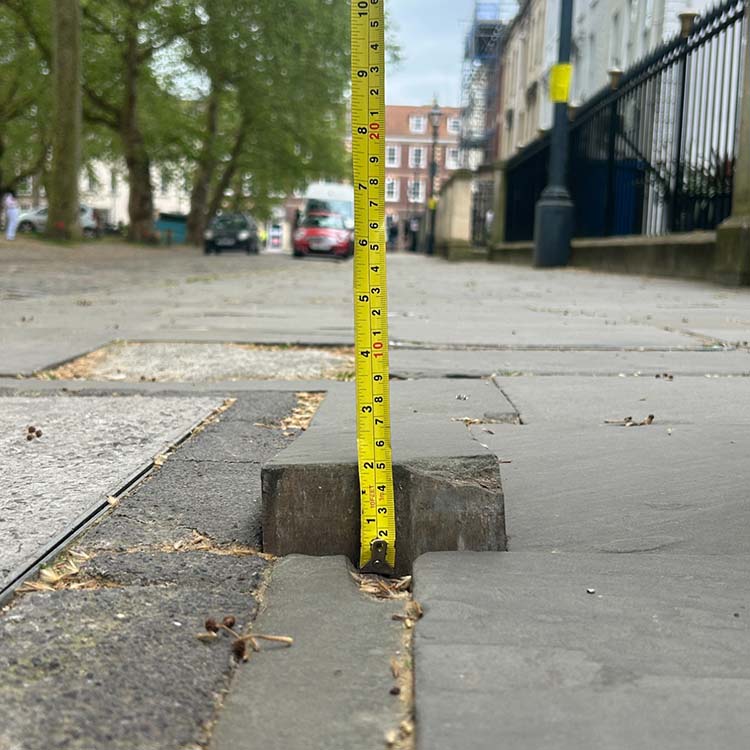 Yellow tape measure measuring the height of a loose paving slab