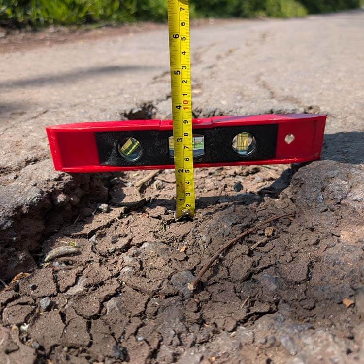 Spirit level and tape measure over a pothole