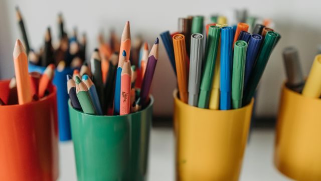 Close-up of colorful pencils and pens in bright plastic holders on a desk