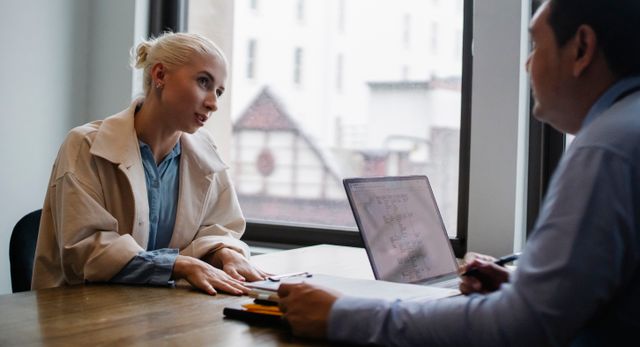 Two professionals engaged in a discussion at an office with a laptop and documents on the table