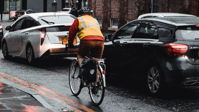 A cyclist with a high-visibility vest rides through a rainy city street