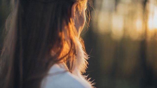 A woman facing away from the camera looking into the distance at sunset