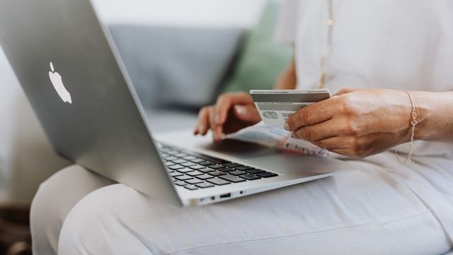 Close-up of a person holding a credit card while using a laptop