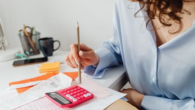 A woman calculating expenses using a calculator and papers at her desk