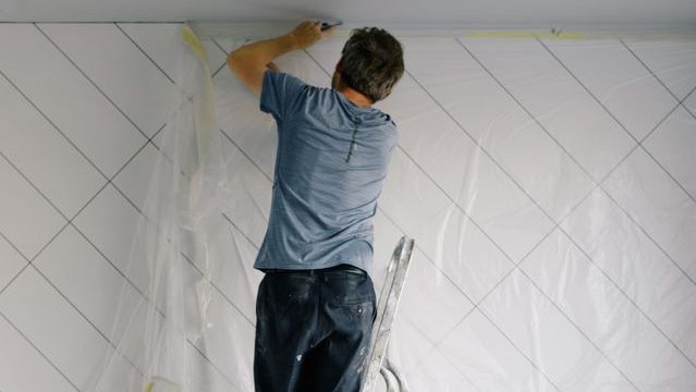 Male decorator on a ladder working indoors to renovate a room