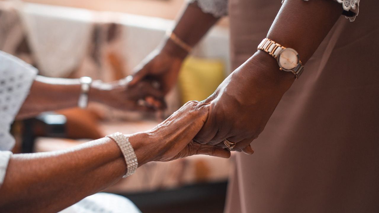 A close-up of an elderly person and a carer holding hands